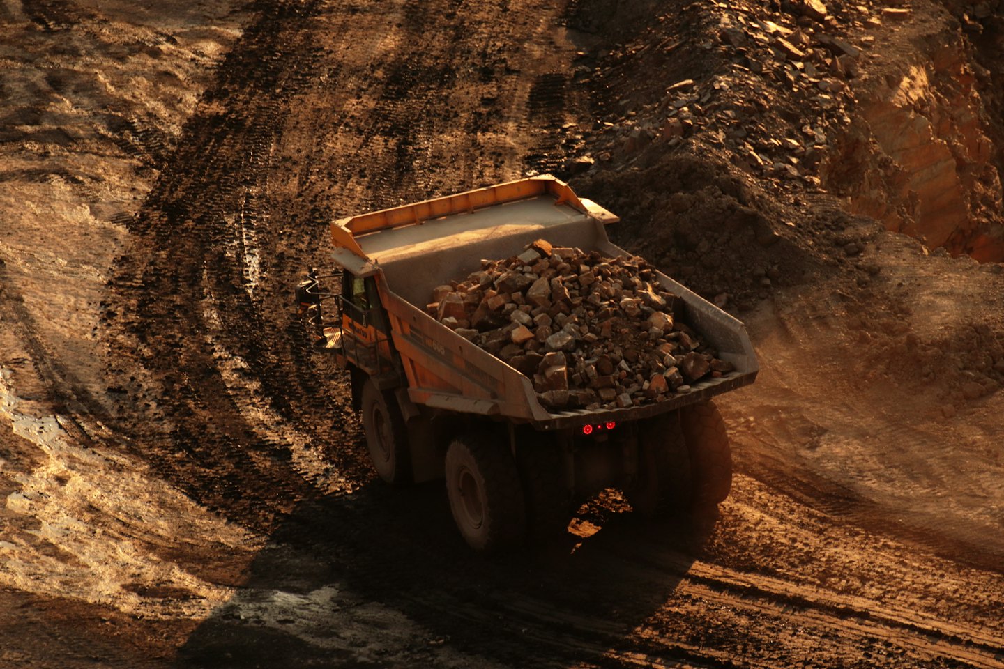 Large orange dump truck loaded with ore on a dirt road.