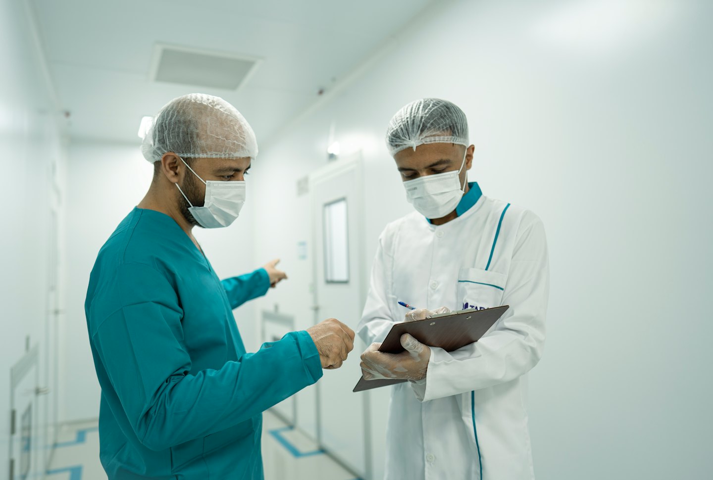 Medical professionals in masks consult in a sterile white corridor.