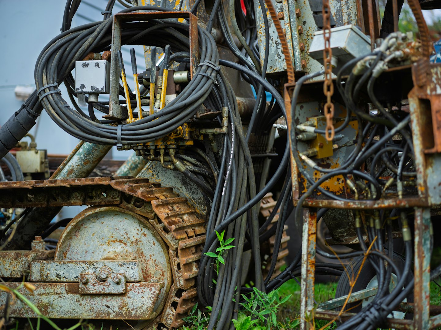 Heavy machinery undercarriage with hydraulic hoses and rusty metal.
